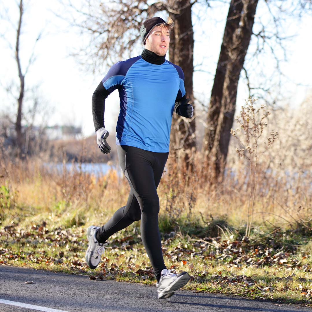 Homem a correr na estrada com equipamento de inverno para se proteger do frio. Tem um gorro uma camisola de manga comprida, luvas e umas leggings para se manter mais quente nos dias frios de inverno.